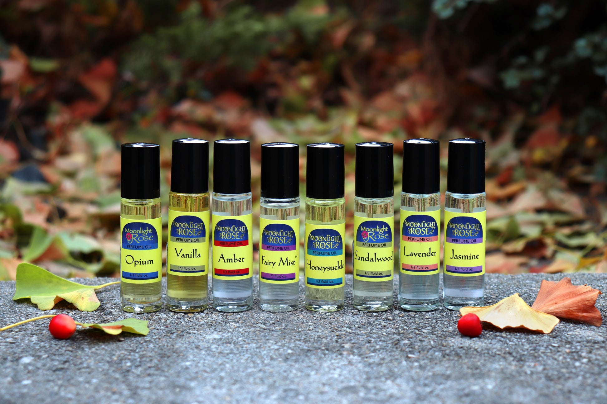 Row of Moonlight Rose roll on perfume bottles with colorful labels on a textured surface with leaves in the background