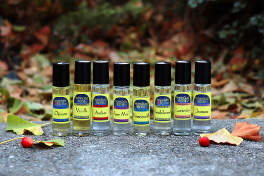 Row of Moonlight Rose roll on perfume bottles with colorful labels on a textured surface with leaves in the background